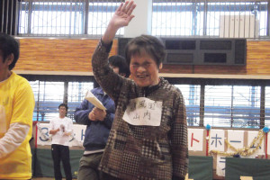 表彰式で笑顔で手を挙げている利用者さん